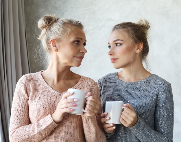 Linda mãe madura e sua filha adulta estão bebendo café conversando e sorrindo