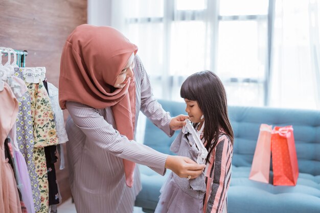 Linda mãe muçulmana fazendo compras com a filha em uma loja de roupas ou pegando uma roupa no armário