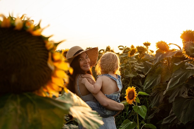 Foto linda mãe segura um filho bebê em um campo de girassol. ternura, sorrisos, felicidade.