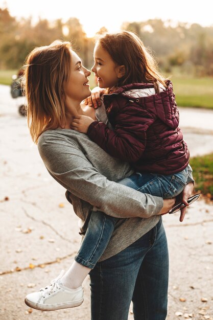 Foto linda mãe segurando nos braços a filha dela, olhando para ela contra o aluno no parque.