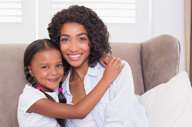 Linda mãe sentada no sofá com a filha sorrindo para a câmera