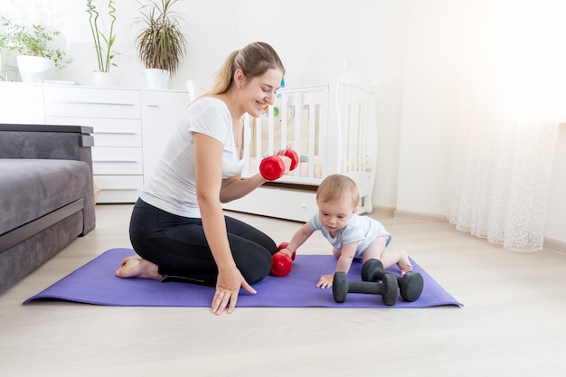 Linda mãe sorridente com seu filho se exercitando no chão com halteres