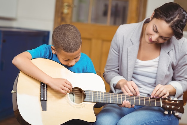 Linda maestra dando clases de guitarra a un alumno en un aula