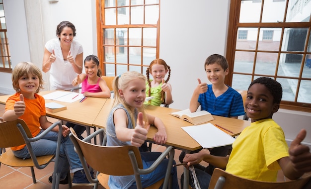 Linda maestra de pie con los alumnos en el escritorio