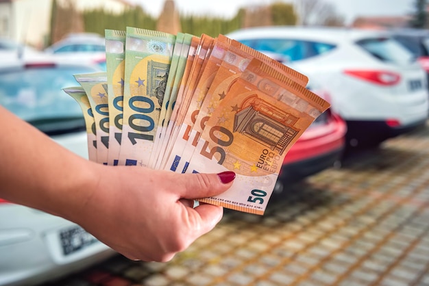 Linda mão segura de bom grado novas notas de euro em um fundo de belos carros novos