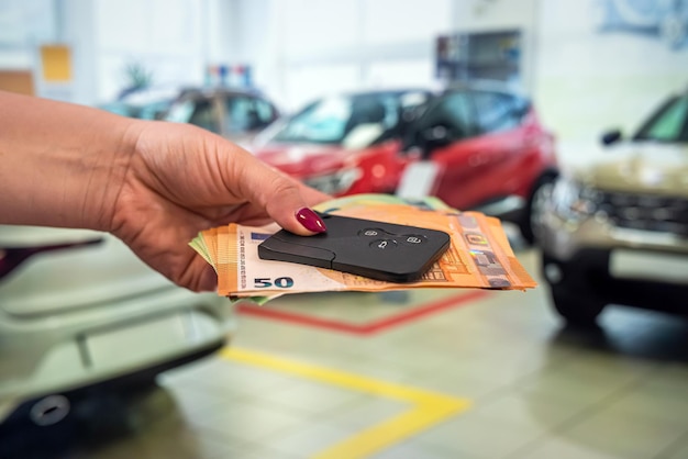 Linda mão segura de bom grado novas notas de euro em um fundo de belos carros novos