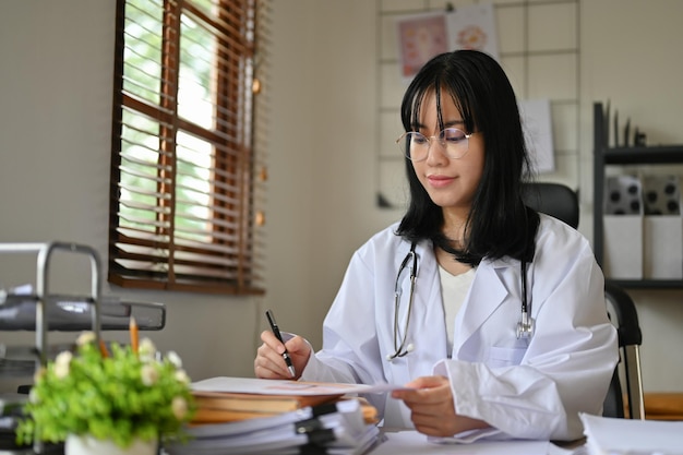 Linda médica asiática de vestido branco está trabalhando em sua mesa