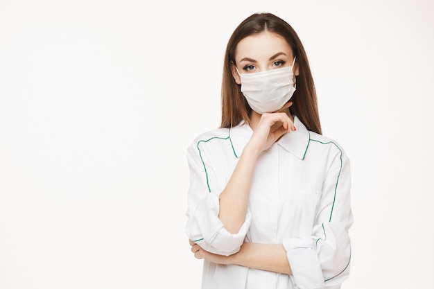 Linda médica ou enfermeira vestindo máscara protetora e posando de vestido médico. Jovem de uniforme médico. Conceito de saúde