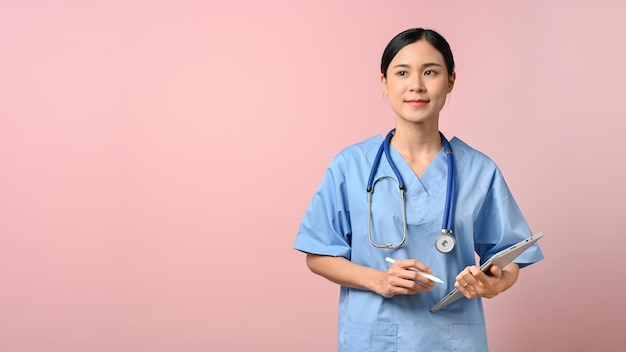 Linda médica segurando o tablet em pé no fundo rosa isolado