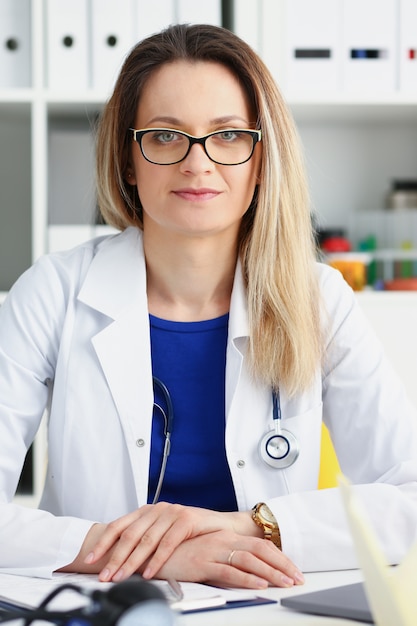 Linda médica sorridente, sente-se no local de trabalho.