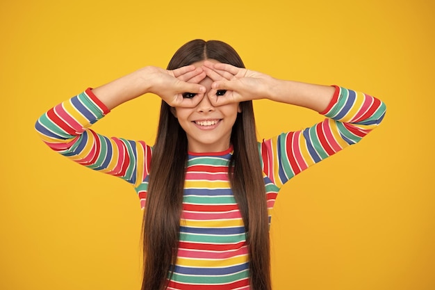 Linda menina adolescente olha especificações de dedos okey símbolo de formas bobas figuras isoladas em fundo amarelo Cara de crianças engraçadas