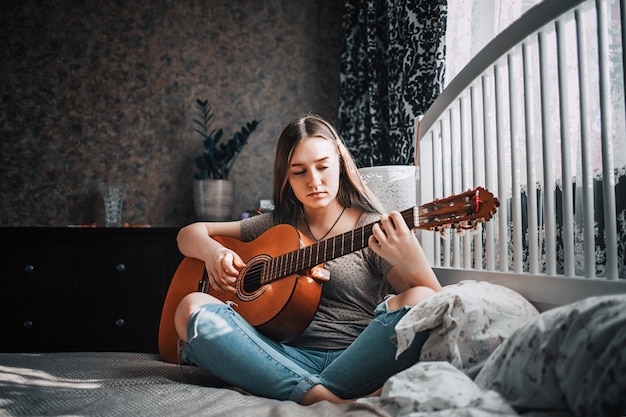 Linda menina adolescente tocando guitarra no quarto dela.