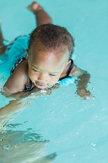 Linda menina aprendendo a nadar na piscina coberta.