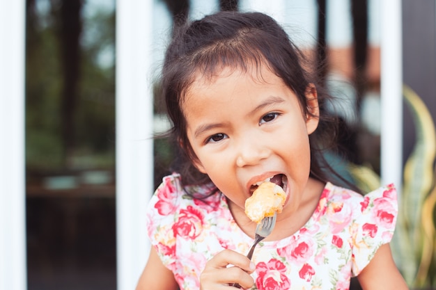 Linda menina asiática criança comendo torradas deliciosas no café da manhã com felicidade