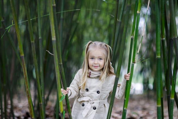 Linda menina com cabelo loiro em pé em uma floresta de bambu e agitando o bambu