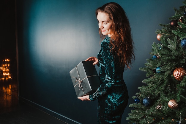 Linda menina com caixa de presente perto de árvore de Natal