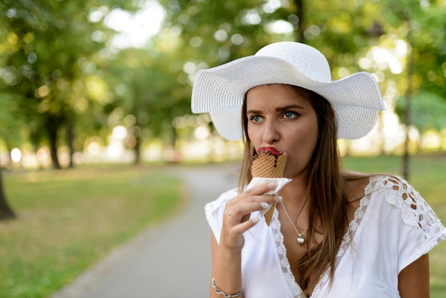 Linda menina com chapéu branco comendo sorvete na rua da cidade