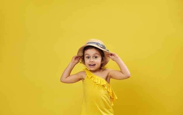 Linda menina com chapéu de verão posa em uma superfície amarela com espaço de cópia expressando emoção