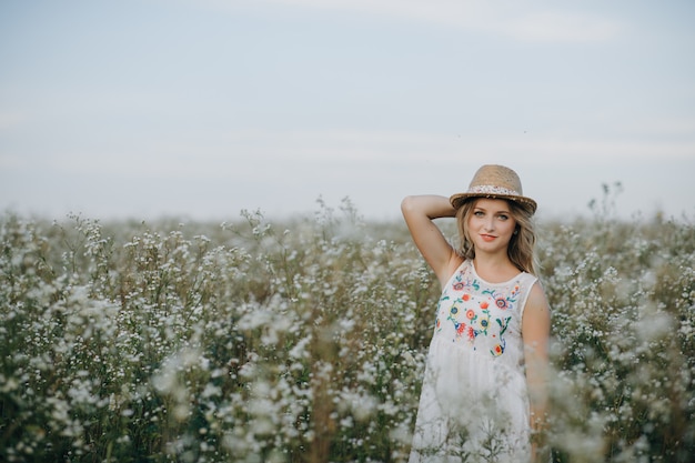 Linda menina com um chapéu na mão entra em um campo com flores do campo e sorri sinceramente