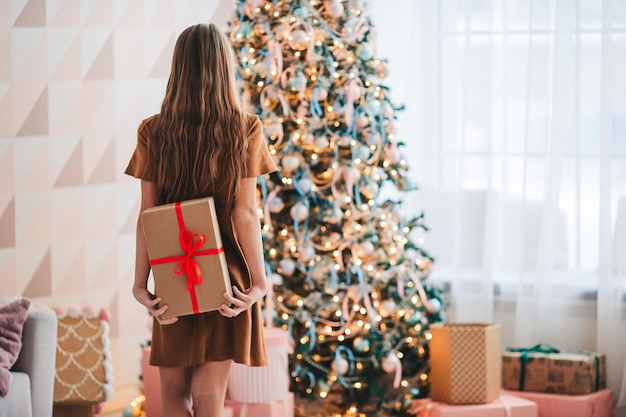 Linda menina com uma caixa de presente perto da árvore de Natal. Feliz Natal e Boas Festas.