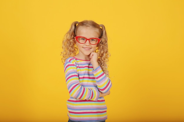 linda menina loira sorridente com óculos em um fundo amarelo em uma jaqueta colorida emoções