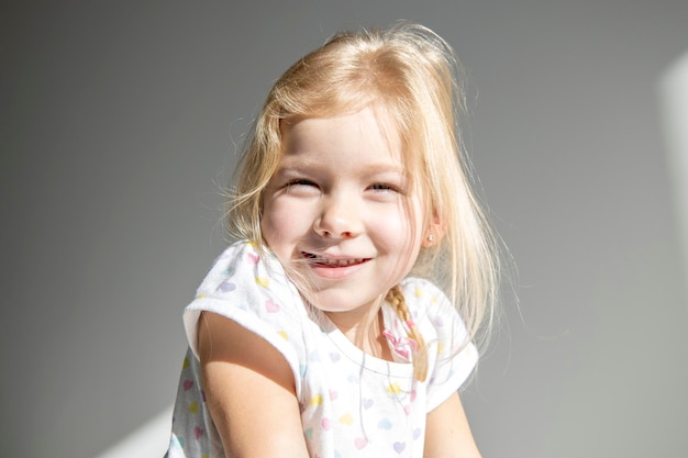 Linda menina loira sorridente no fundo de uma parede branca