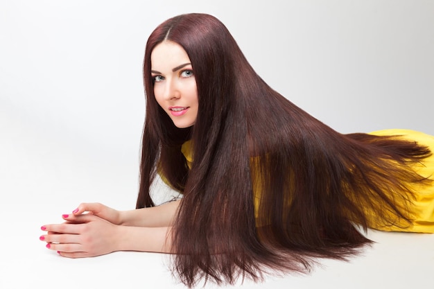 Linda menina morena com cabelo escuro longo e saudável em vestido amarelo posando no estúdio