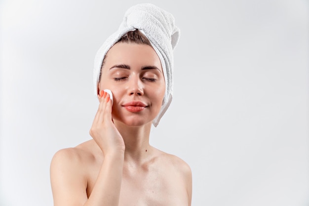 Linda menina morena com uma toalha branca esfregando o rosto em um fundo branco