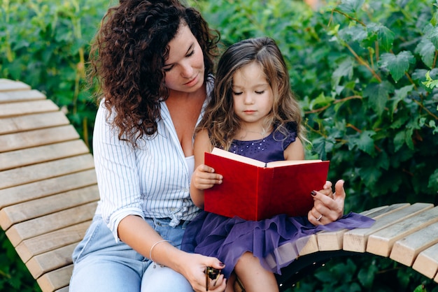 Linda, menina, segurando um livro, sua mãe ajuda a menina a ler, ao ar livre