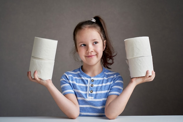 Linda menina sentada à mesa e papel higiênico em falta