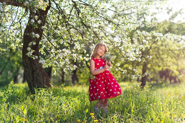 Linda menina sentada sob uma árvore com um buquê de flores silvestres nas mãos