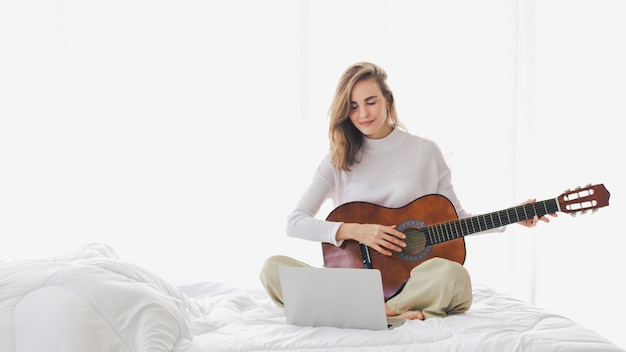 Linda menina sentada tocando violão na cama no quarto