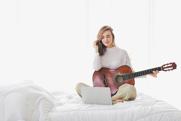 Foto linda menina sentada tocando violão na cama no quarto