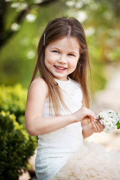 Foto linda menina sorridente com vestido creme, contra o verde do parque de verão