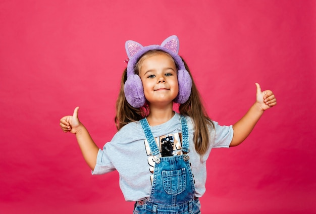 Linda menina sorridente se divertindo em fones de ouvido de pele em um fundo rosa.