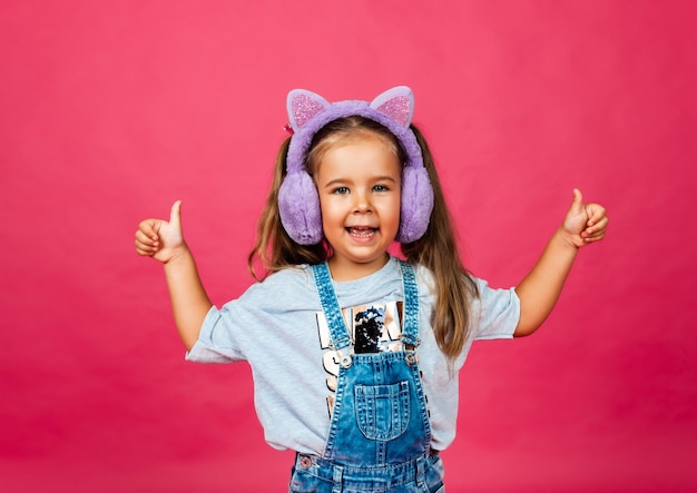 Linda menina sorridente se divertindo em fones de ouvido de pele em um fundo rosa.