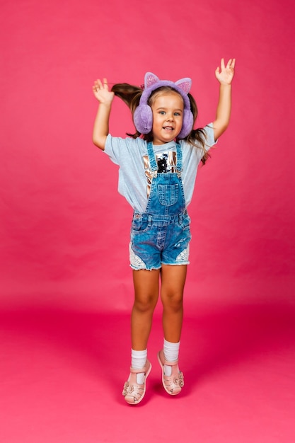 Linda menina sorridente se divertindo em fones de ouvido de pele em um fundo rosa.