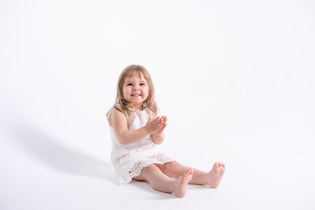 Linda menina vestida de branco, sentada no fundo branco.