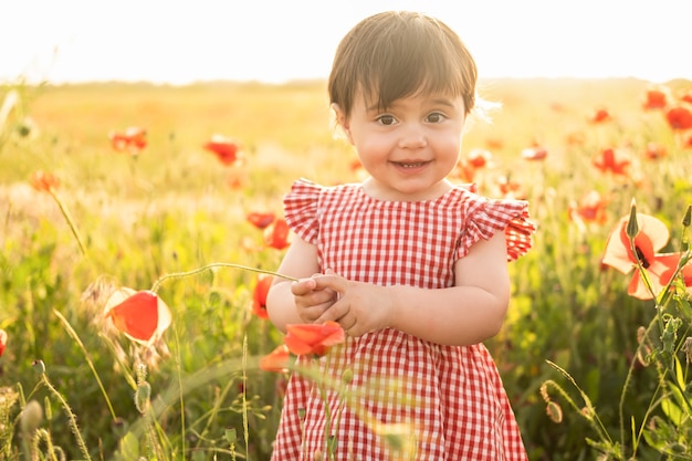 Linda menina vestida de vermelho em campo de papoulas ao pôr do sol de verão