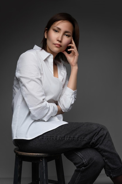 Linda modelo asiática vestindo uma camisa branca enorme e posando no estúdio fotográfico