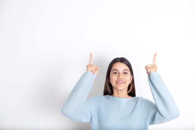 Foto una linda morena adolescente de fondo blanco señala con los dedos hacia arriba un lugar para el anuncio de texto