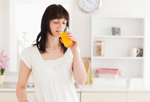 Linda morena bebendo um copo de suco de laranja enquanto está de pé