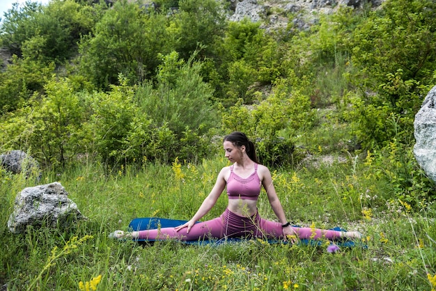 Linda morena bonita em um top de framboesa e leggings perto da rocha estica seu corpo para a saúde do corpo O conceito de alongamento na natureza