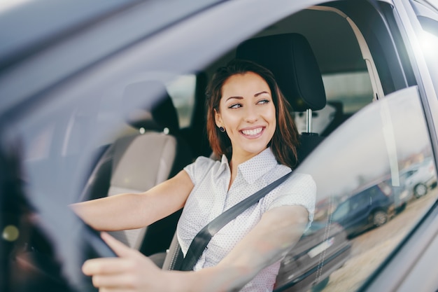 Linda morena caucasiana sorridente, dirigindo o carro dela.