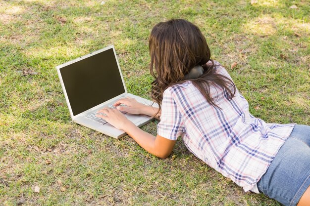 Linda morena deitada na grama e usando laptop