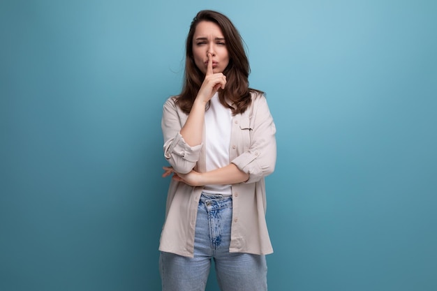 Linda morena jovem adulta de camisa e jeans mantém um segredo sobre fundo azul