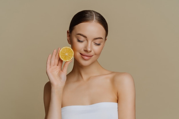 Linda morena jovem concentrada segurando uma fatia de limão fresco e recomendando beleza natural