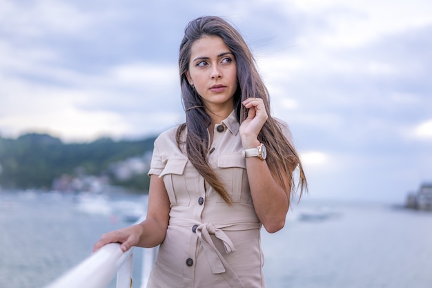 Linda morena jovem posando perto do mar durante o tempo ventoso em San Sebastian, Espanha