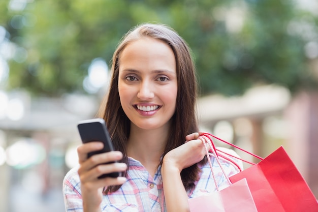 Linda morena sorrindo na câmera e segurando um smartphone