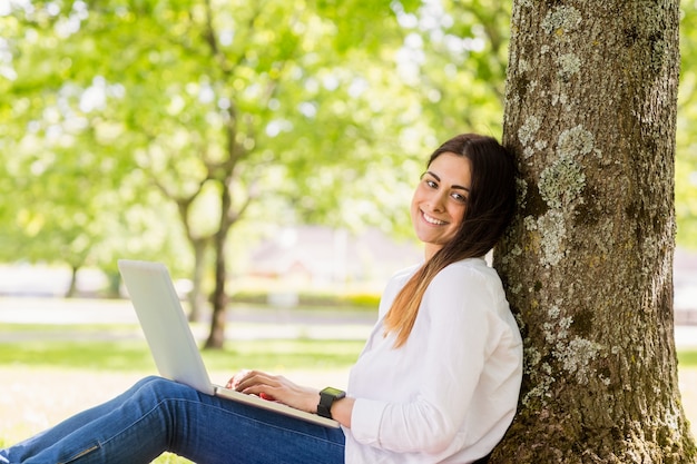 Linda morena usando o laptop no parque